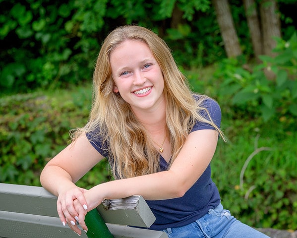 high school senior girl leaning on a bench at her senior portrait session at a park in bourne