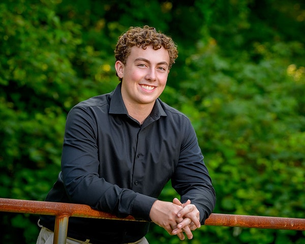 high school senior boy leaning on a gate for his senior portrait in a park in bourne near plymouth
