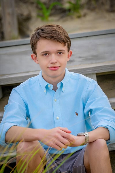senior boy sitting on steps at sagamore beach posing for yearbook photo