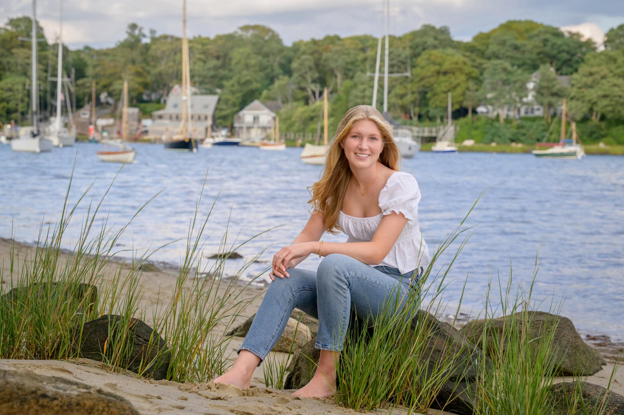 quisset harbor senior session senior girl sitting on a rock at Quisset Harbor with sailboats in the background